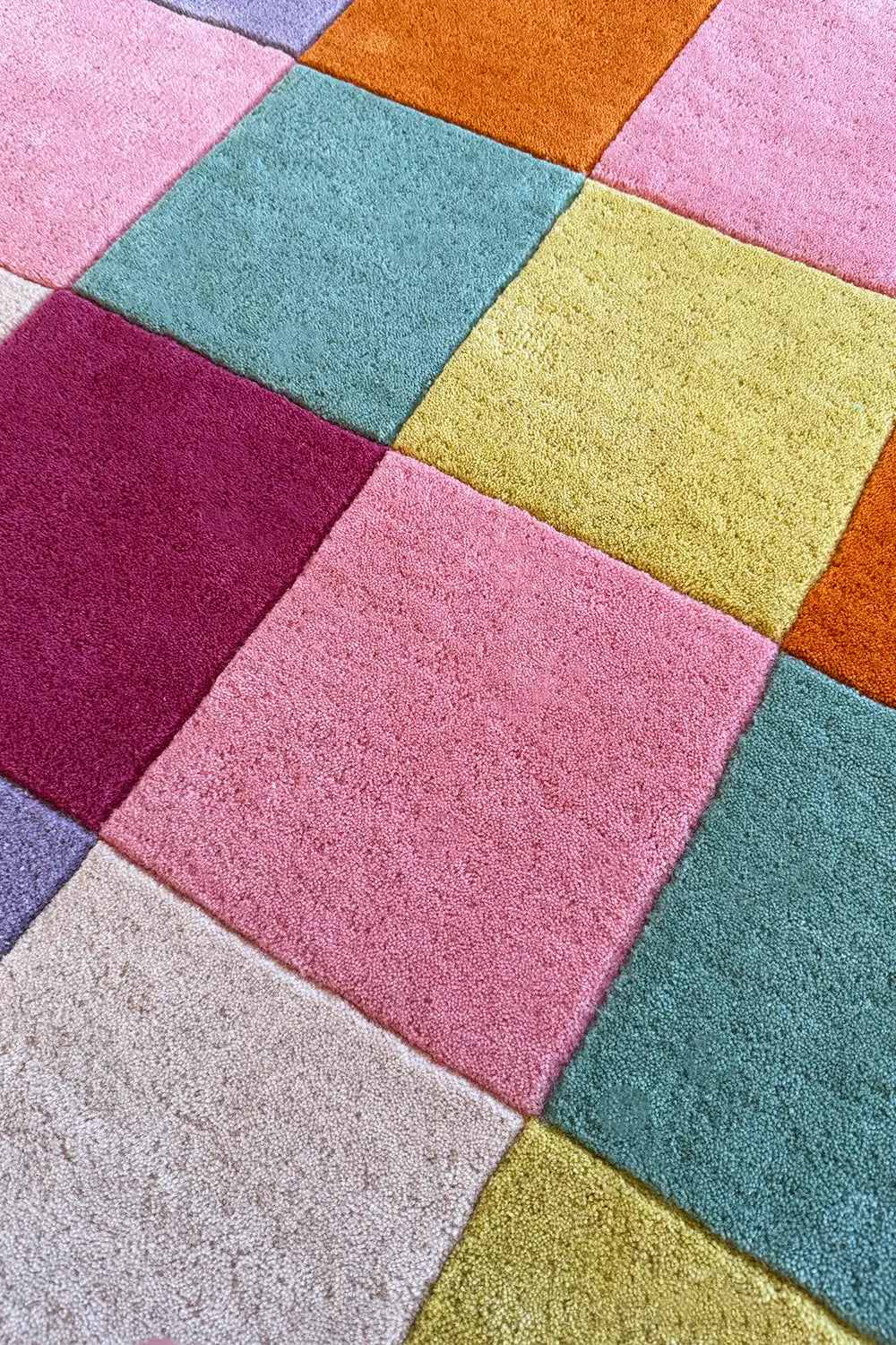 Detail view of round colorful checkered wool rug with soft pastel and vibrant color blocks