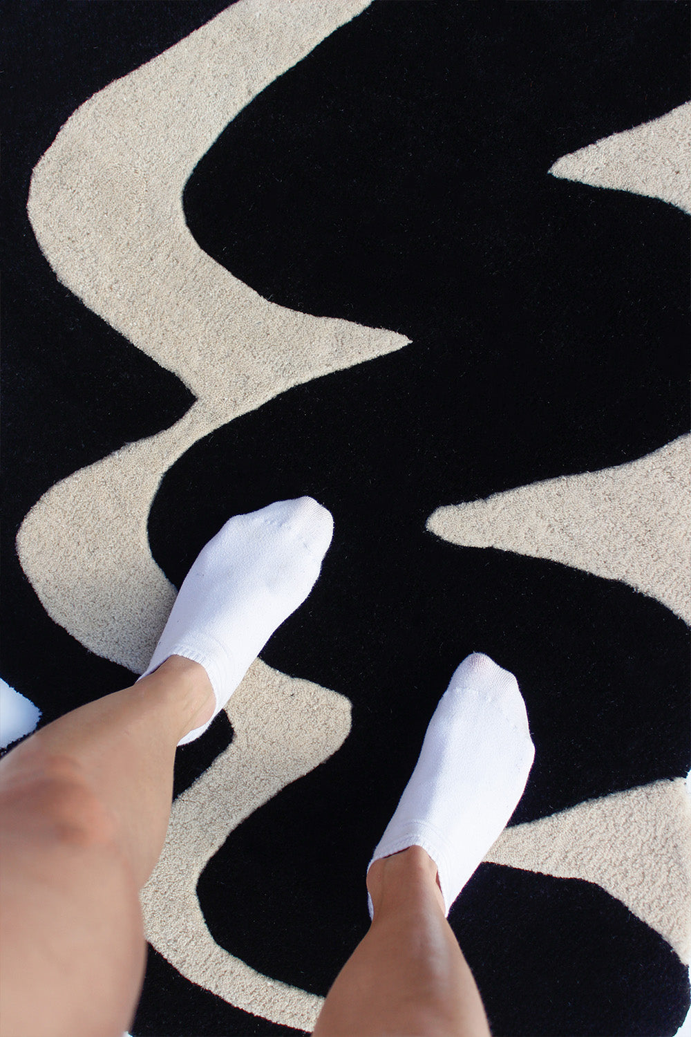 Person standing on black and ivory irregular rug with wavy design