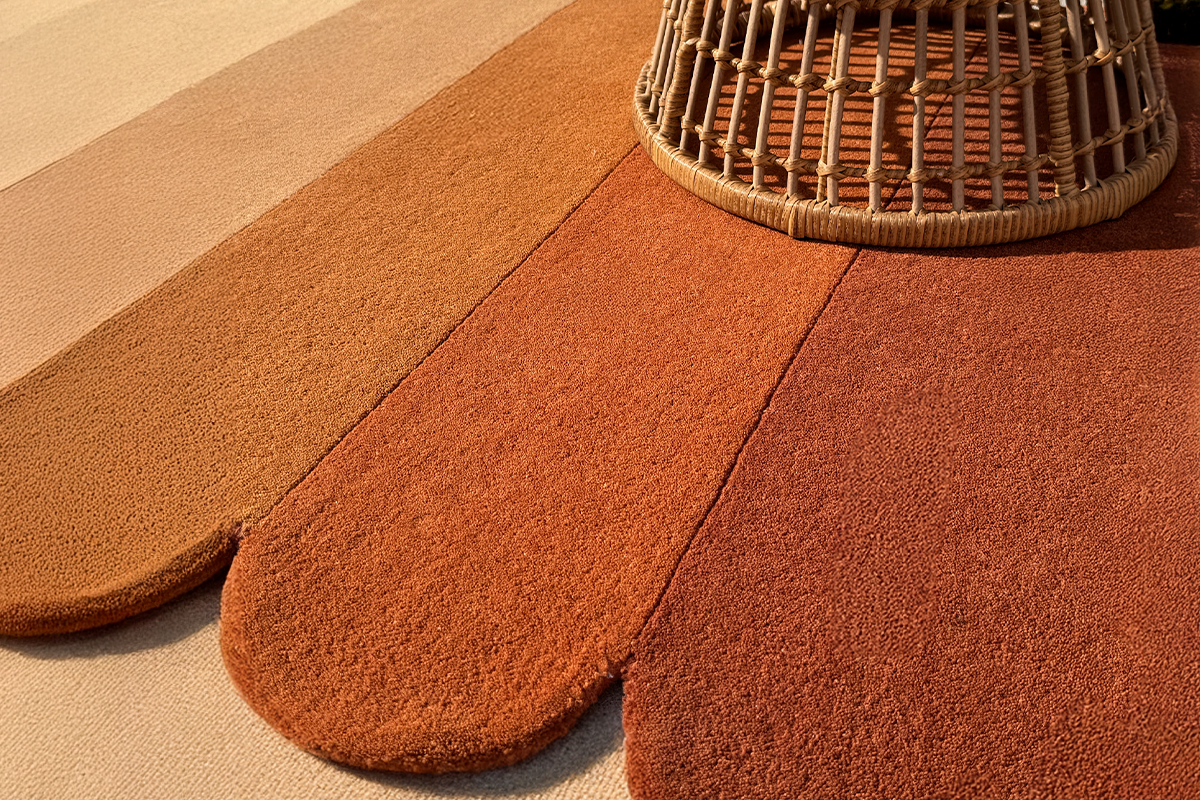 modern gold and burnt orange scalloped wool rug in a boho room under rattan chair