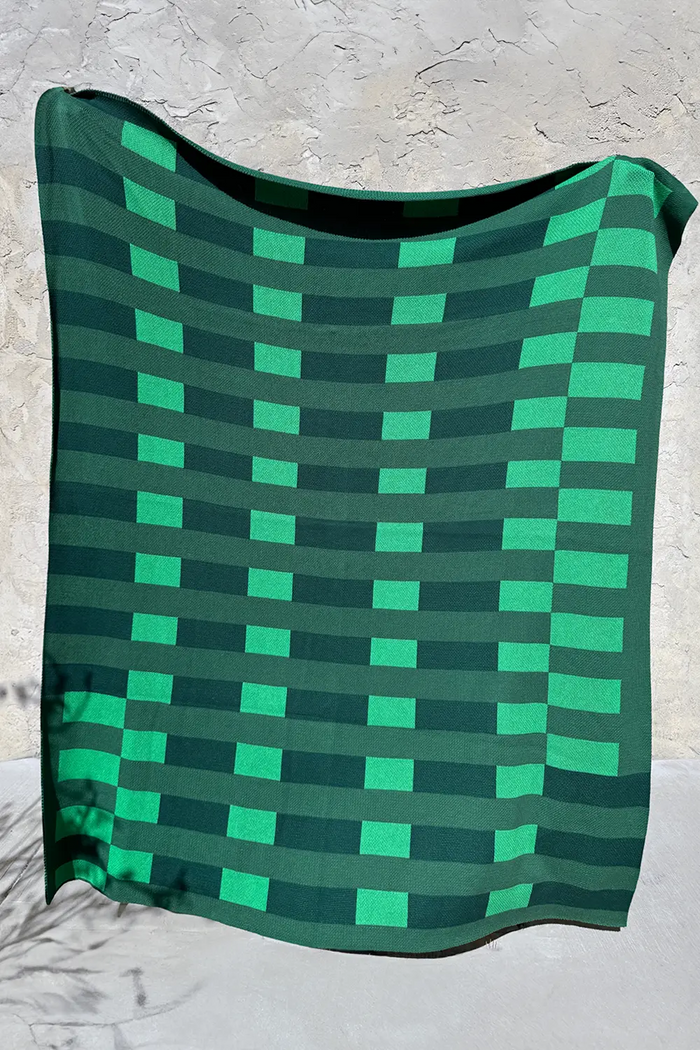 Green knit throw blanket with a modern geometric striped checkerboard pattern.
