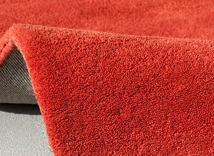 Close-up of a textured red rug corner on a neutral background