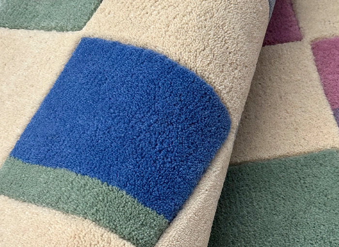 Close-up of a textured rug with blue, green, and purple squares.