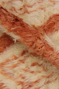 Detail of plush high-pile wool shag rug featuring hand-dyed burnt orange diamond patterns, ideal for cozy living rooms or layered boho interiors