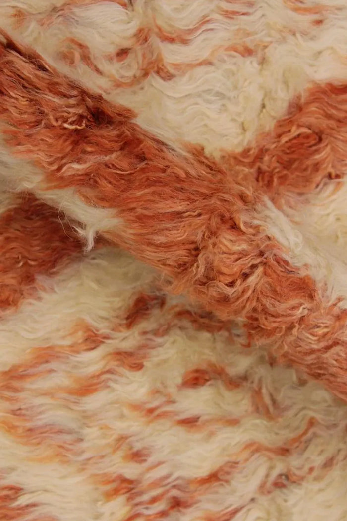 Detail of plush high-pile wool shag rug featuring hand-dyed burnt orange diamond patterns, ideal for cozy living rooms or layered boho interiors