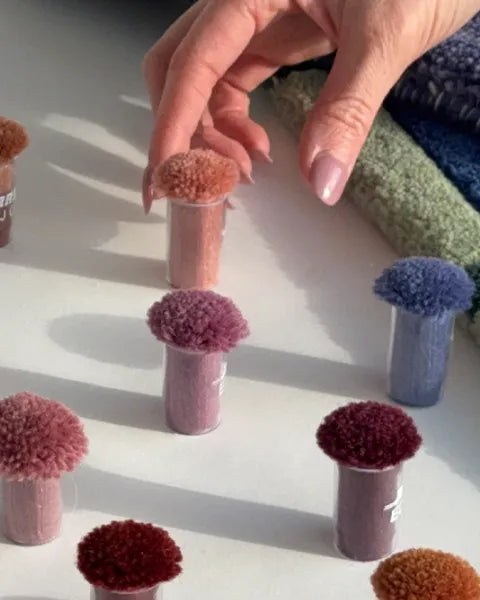 Hand interacting with colorful pom-pom decor items on a light surface