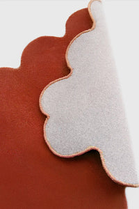 Orange terracotta scalloped edge wool rug folded to reveal cotton backing and sculpted hand-carved shape burnt orange