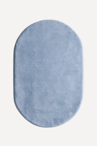 A light blue oval plush rug with a soft, textured surface, shown from a top-down view on a clean off-white background.