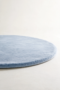 close up of a round baby blue rug shown from a low angle highlighting its soft plush pile