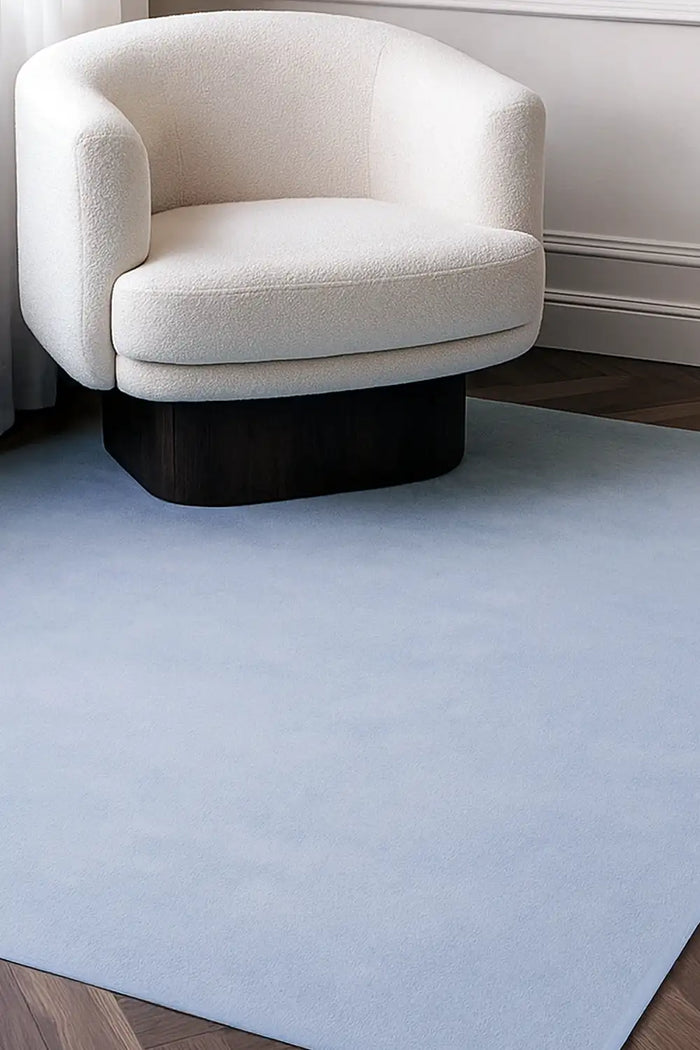 Light blue wool rug in 8x10 size styled under a cream armchair, perfect for minimalist living rooms or bedroom rugs lifestyle