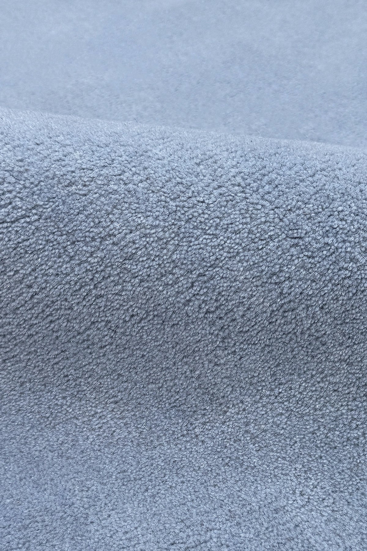 A close-up of a textured blue oval rug muted light blue-gray color, showing the pile and weave detail.