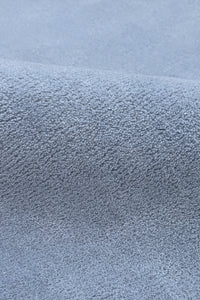 A close-up of a textured blue oval rug muted light blue-gray color, showing the pile and weave detail.