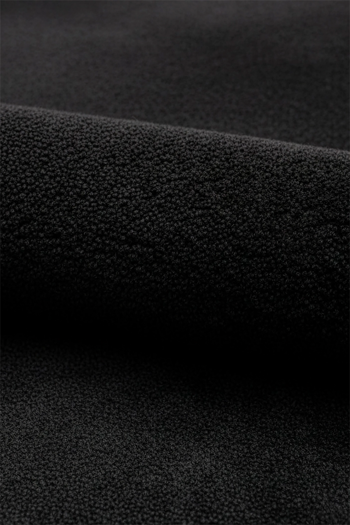 A close-up of a black oval wool rug, shown folded to highlight its tactile quality.