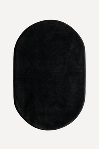 A black oval plush rug with a soft, fuzzy texture, shown from a top-down view on a light off-white background.