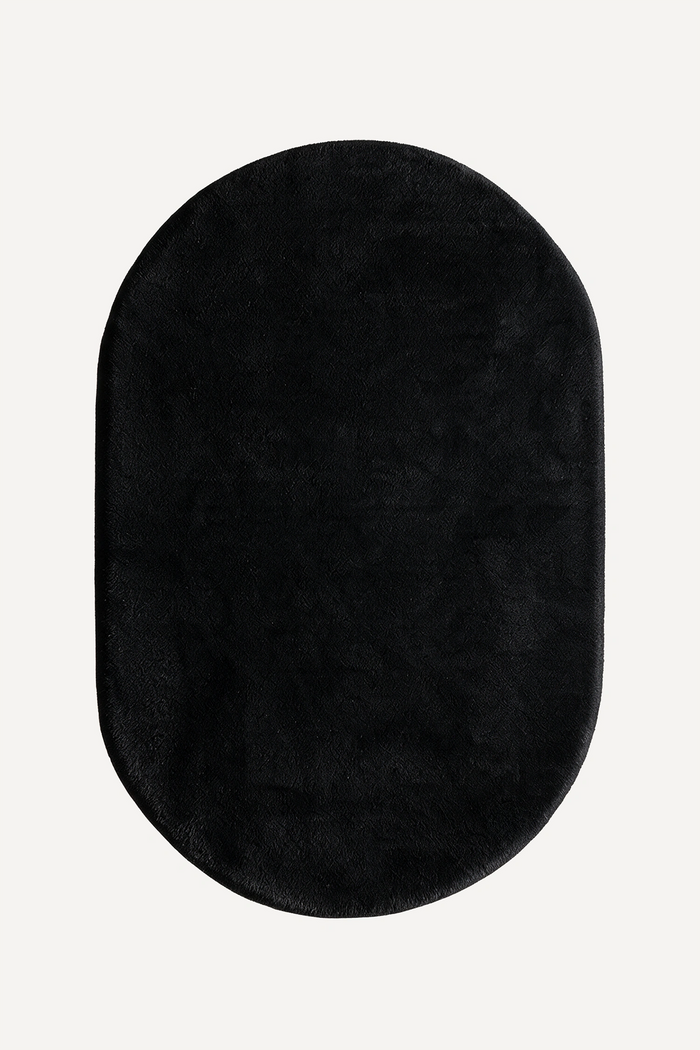 A black oval plush rug with a soft, fuzzy texture, shown from a top-down view on a light off-white background.