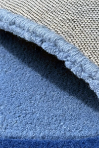 Close-up of blue tufted wool rug with rounded edge binding, handmade luxury rug crafted from New Zealand wool
