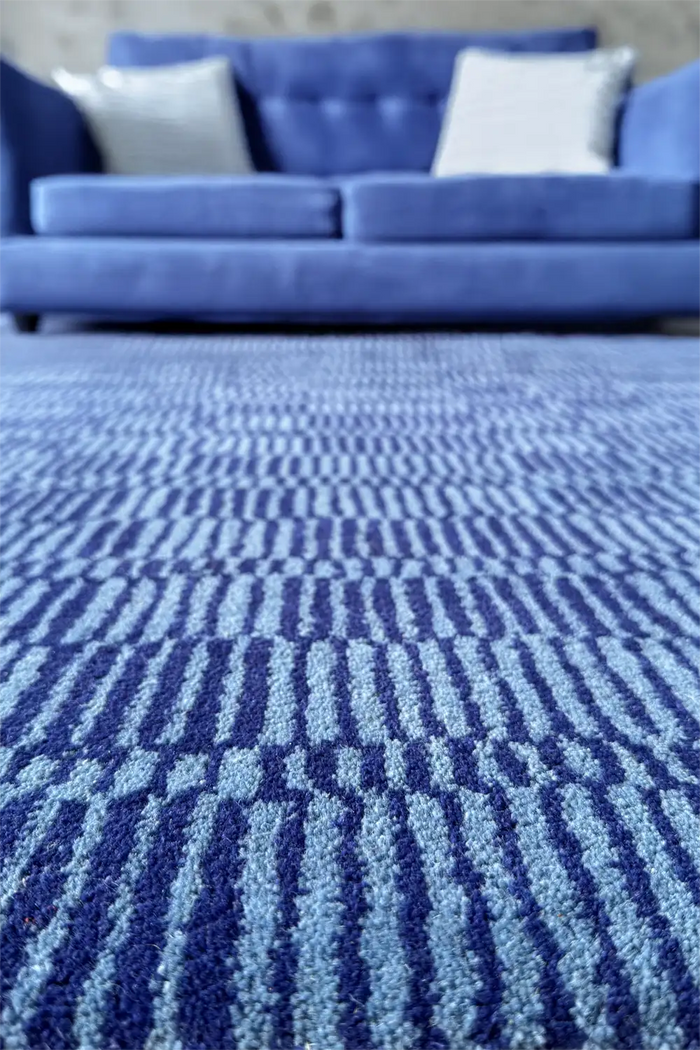 Navy blue area rug styled in a modern grey and blue living room with blue sofa and abstract graphic design