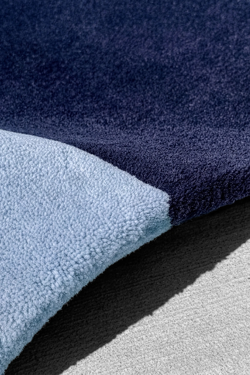 Close-up of two tone wool rug, one side dark blue and one light blue, on a neutral background indigo