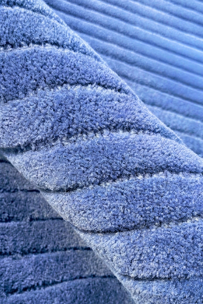 A close-up of a blue ribbed rug with a plush, textured surface, showing the detailed weave and folds.
