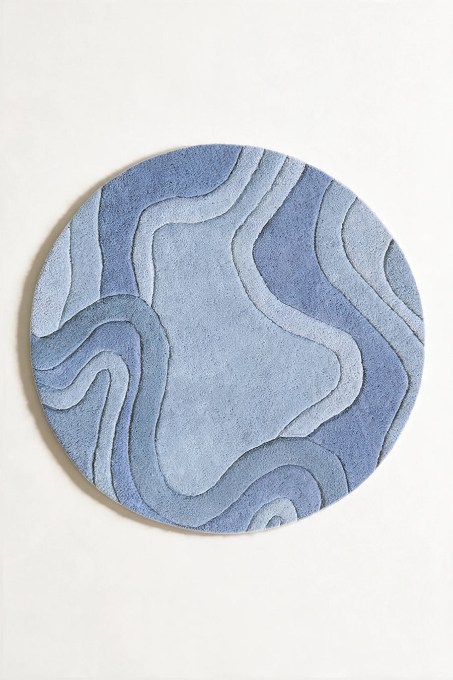 A round area rug featuring an abstract, layered topographic pattern in various shades of blue and light gray, shown against a plain light gray background.