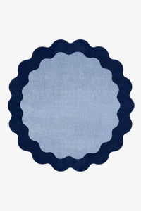 A round rug with a scalloped edge, featuring a light blue center and a dark navy blue border, shown flat against a white background.
