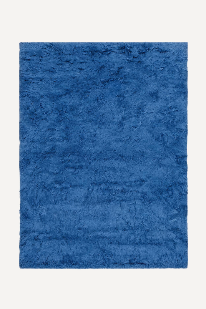 A rectangular blue shag rug with a thick, fluffy texture, shown flat against a light off-white background.