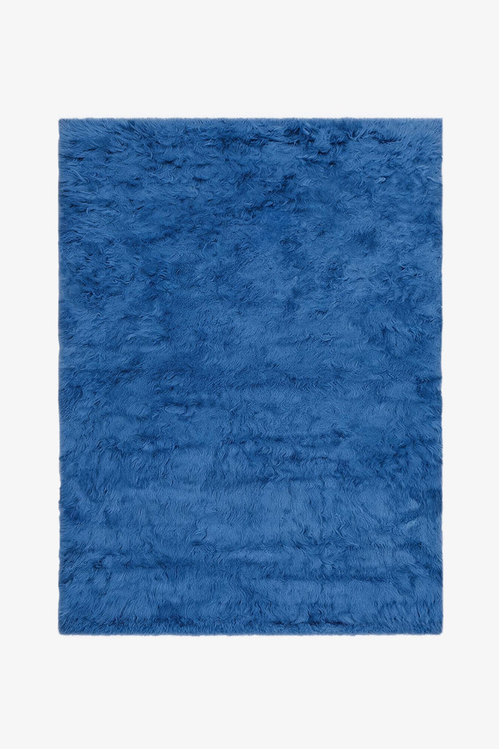 A blue shag rug with a thick, fluffy texture, shown flat against a plain white background.