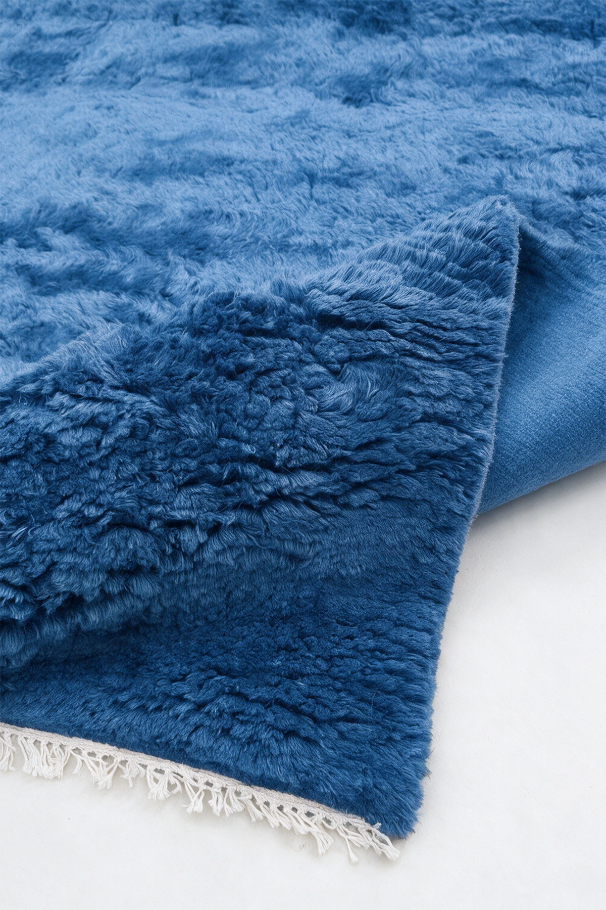 close up texture of a blue shaggy area rug with white fringe