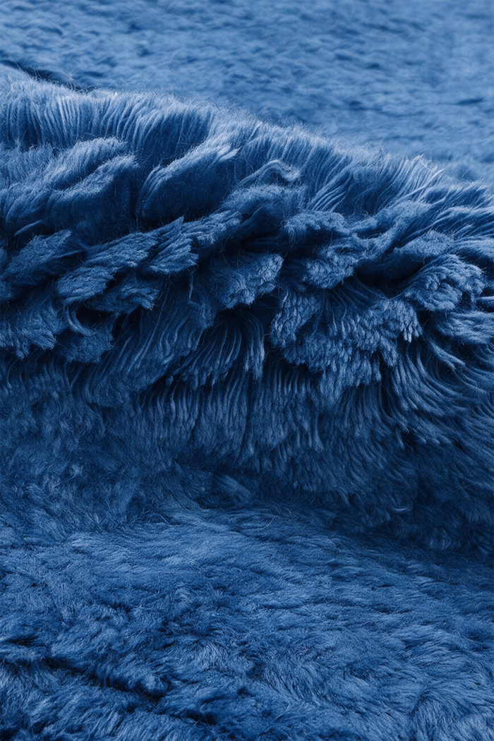 A close-up of a plush, shaggy blue wool rug with dense, fluffy fibers filling the frame.