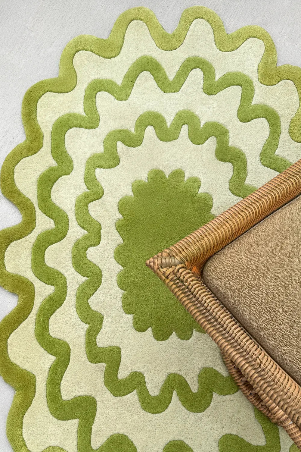 Oval green and ivory wavy rug under a rattan chair, organic modern bohemian rug style.