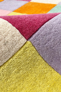Detail of vibrant patterned wool area rug showing colorful tufted squares and hand-finished seams