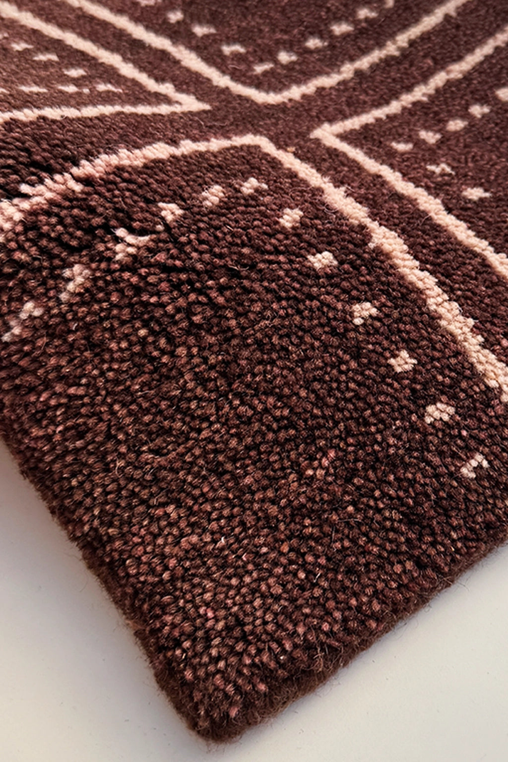 A close-up of a textured, hand-knotted rug with a dark brown base and light beige geometric patterns.