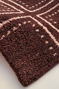 A close-up of a textured, hand-knotted rug with a dark brown base and light beige geometric patterns.