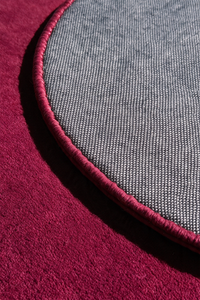 close up view of a burgundy pink round rug backing and binding