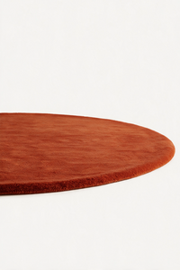 A close-up of a round rust burnt orange rug with a short pile texture, shown against a plain white background.