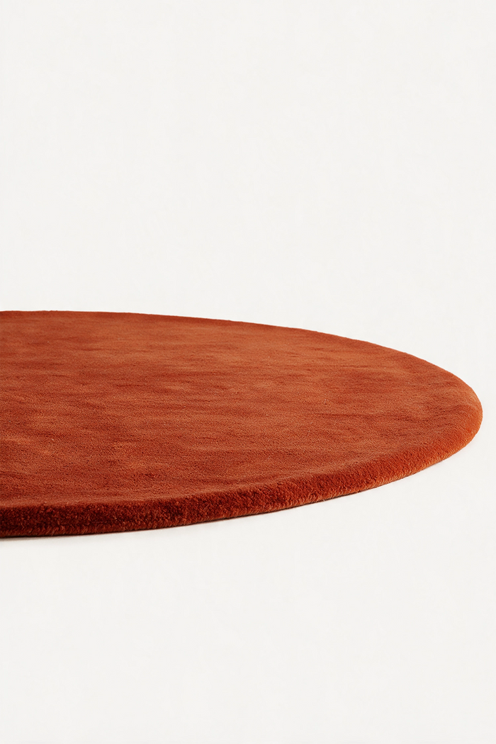 A close-up of a round rust burnt orange rug with a short pile texture, shown against a plain white background.