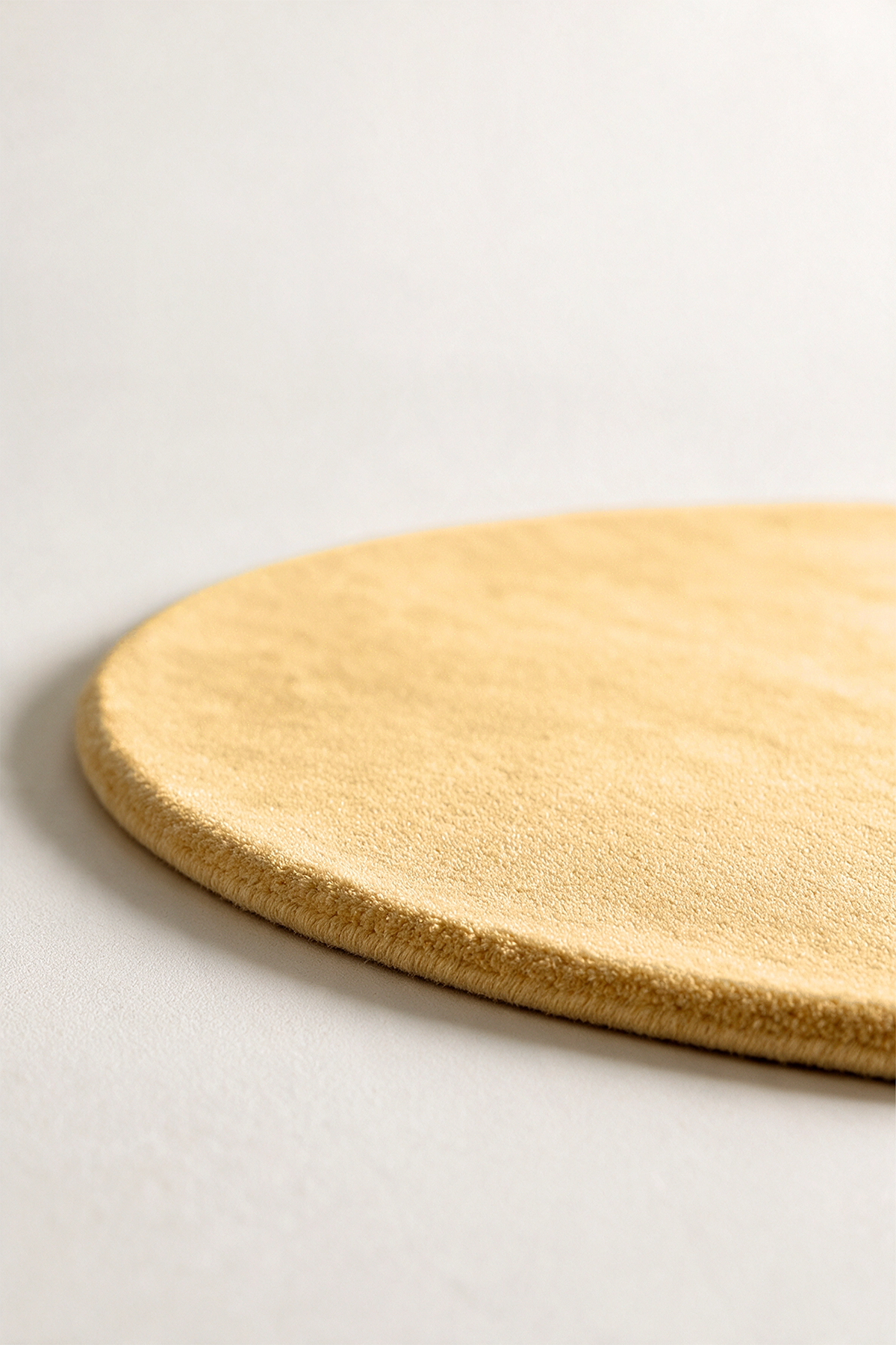 an oval rug shown from a low angle showcasing its butter yellow wool surface and edge binding