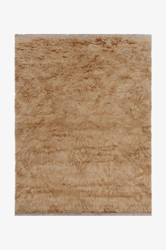 A rectangular shag rug in a warm tan camel shade, shown flat against a plain white background.