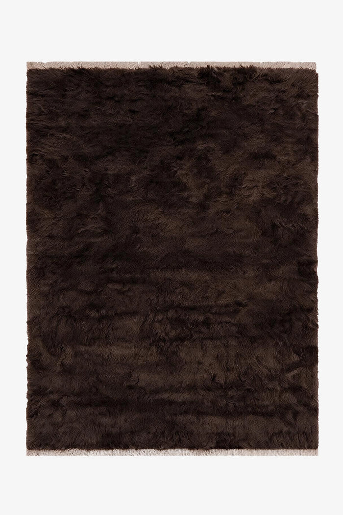 A dark brown shaggy area rug with a textured, fluffy pile and fringed edges, shown flat against a plain white background.