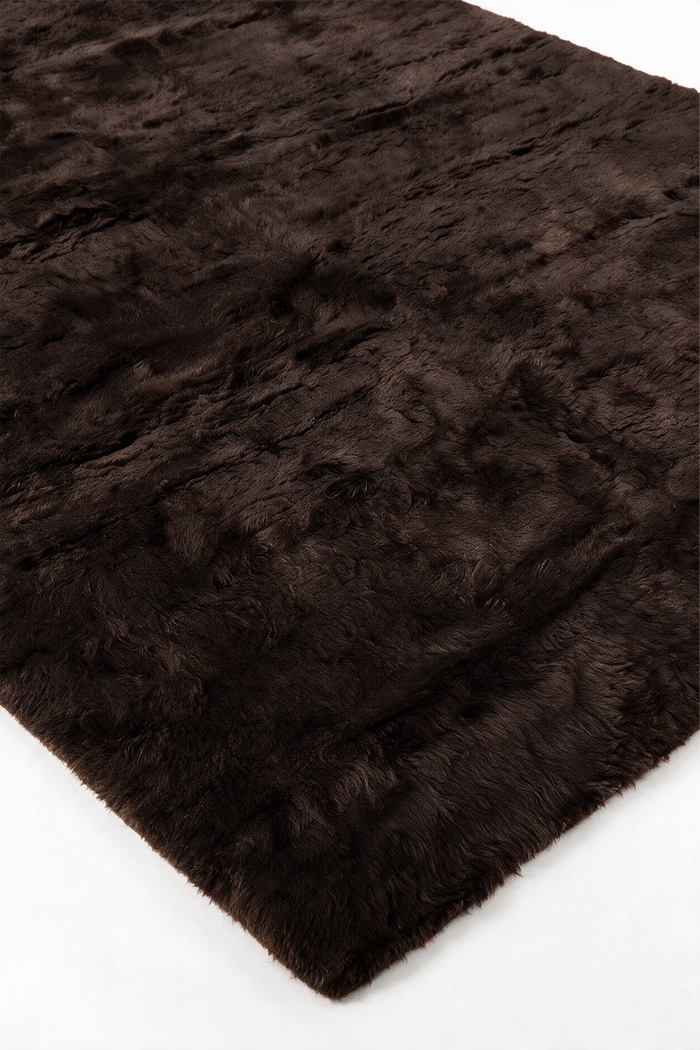 A close-up of a dark chocolate brown shaggy wool rug, showing its thick, plush texture and soft pile on a clean white background.