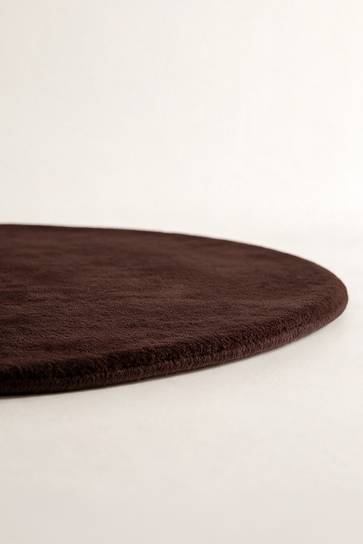 A close-up of a dark chocolate brown oval rug with a plush, textured surface, shown on a clean off-white background.
