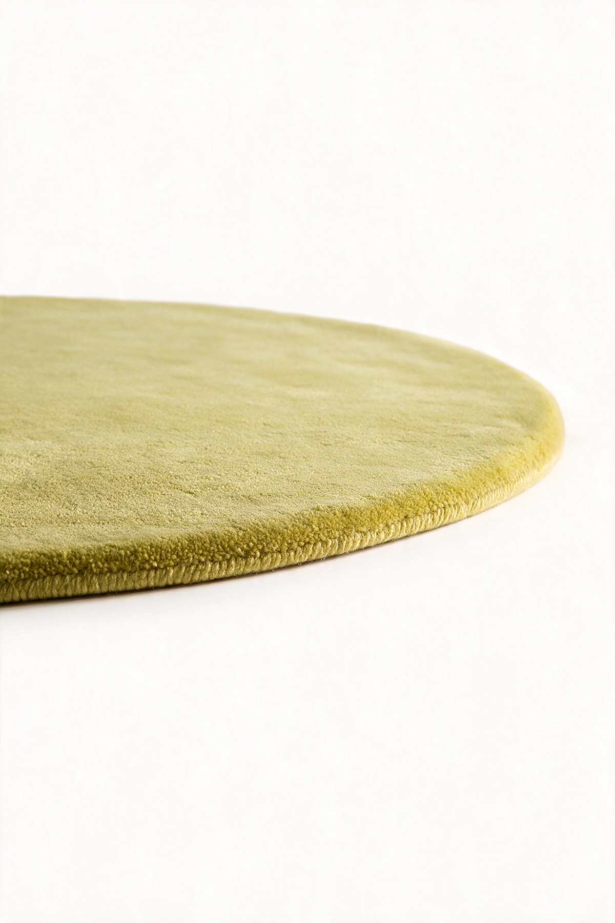 A close-up of an oval area rug in a muted citron color, showing its plush texture and rolled edge against a plain white background.