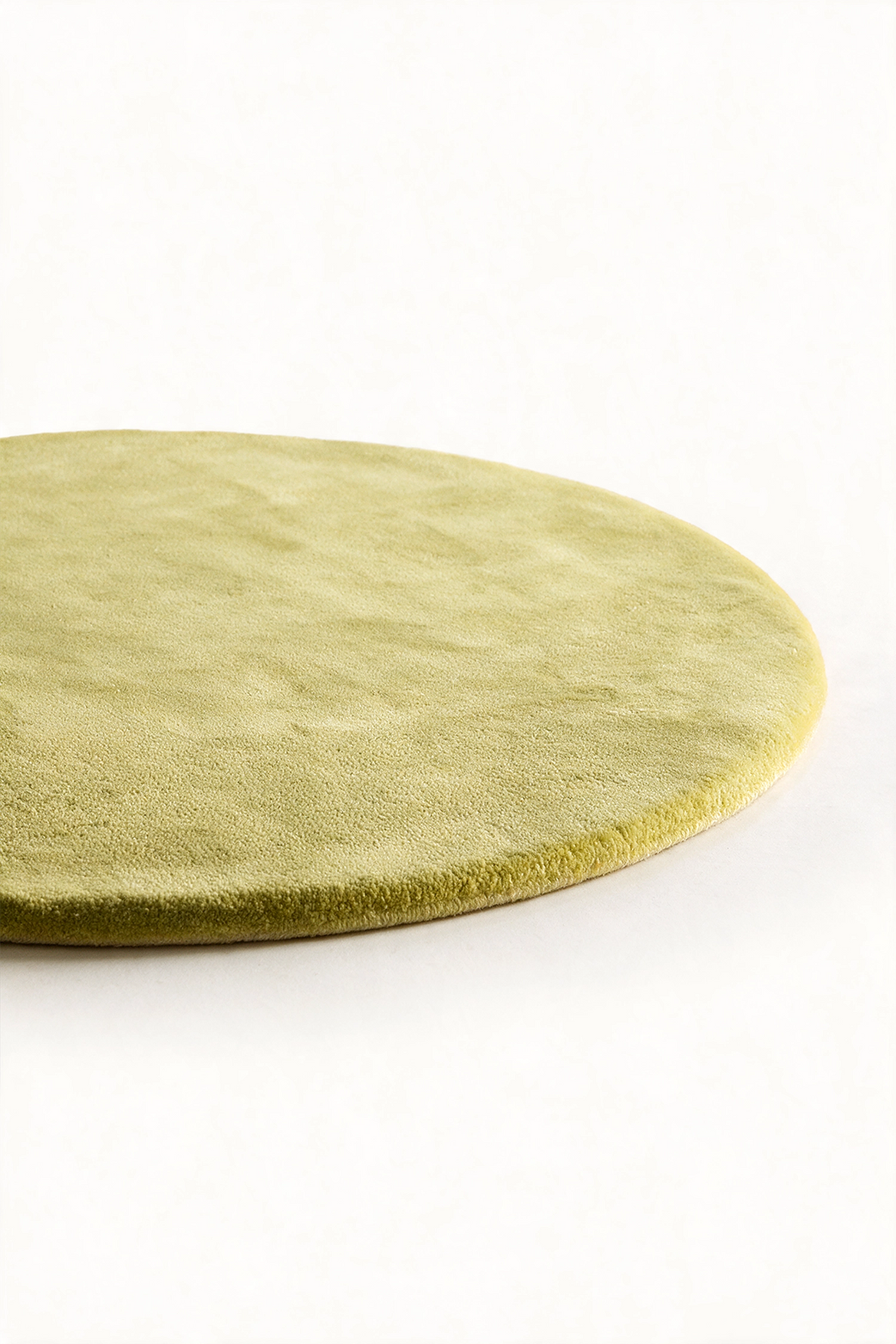 A close-up of a round, light citron green rug with a soft, textured surface, shown on a clean white background.