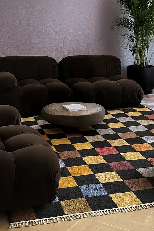 Modern living room with a dark brown sectional sofa and a colorful checkered rug.