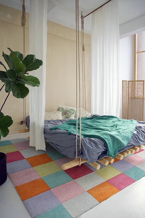 Room with colorful checkered rug, bed with green and blue bedding, and hanging swing.