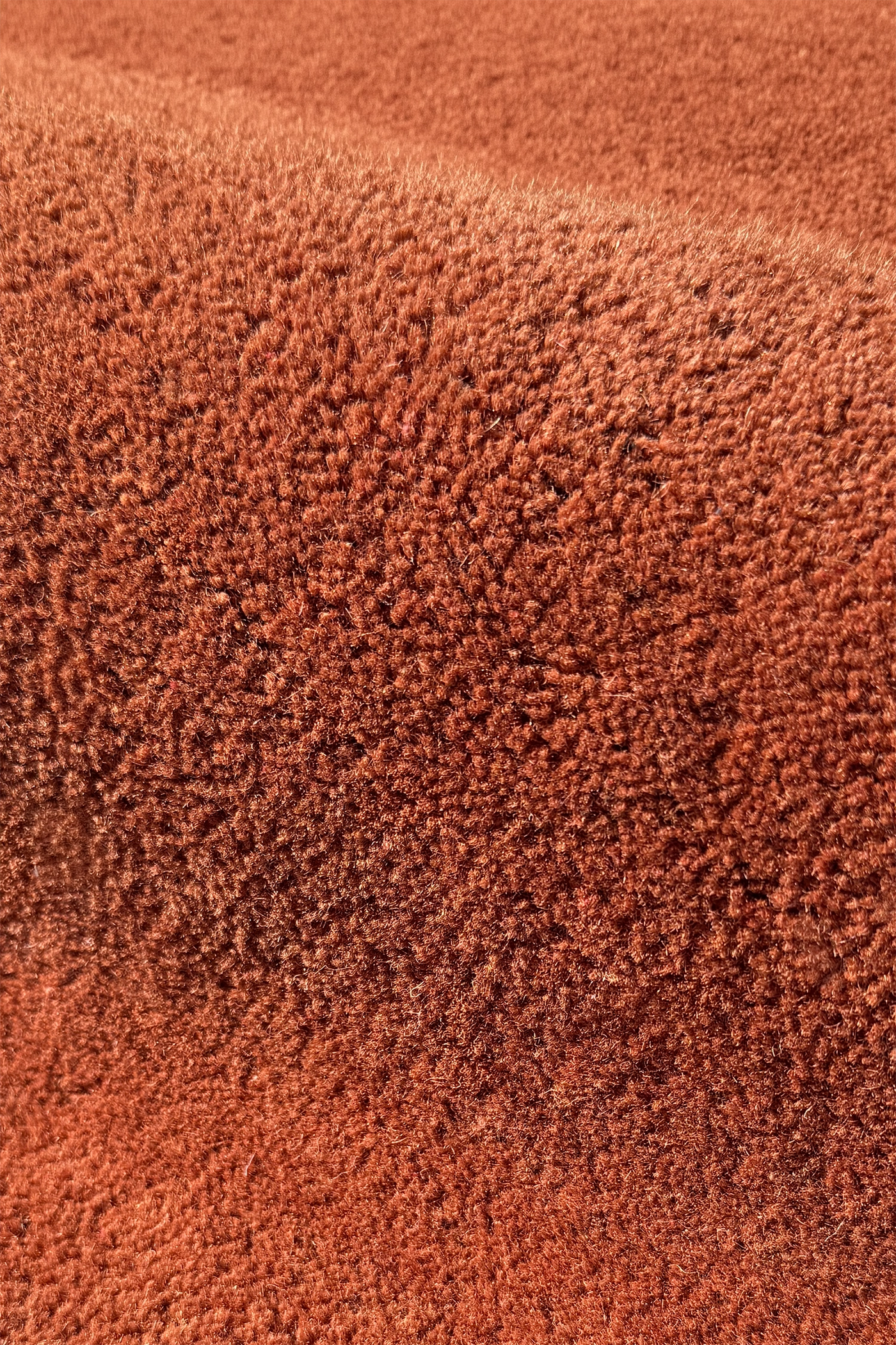 A close-up of a textured terracotta or rust-colored wool rug, showing the dense pile and soft folds brown