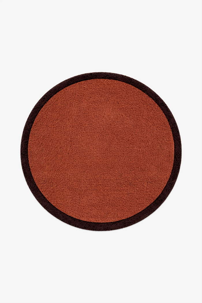 A round wool rug with a rust-orange textured center and a dark brown border, shown flat against a light gray background.