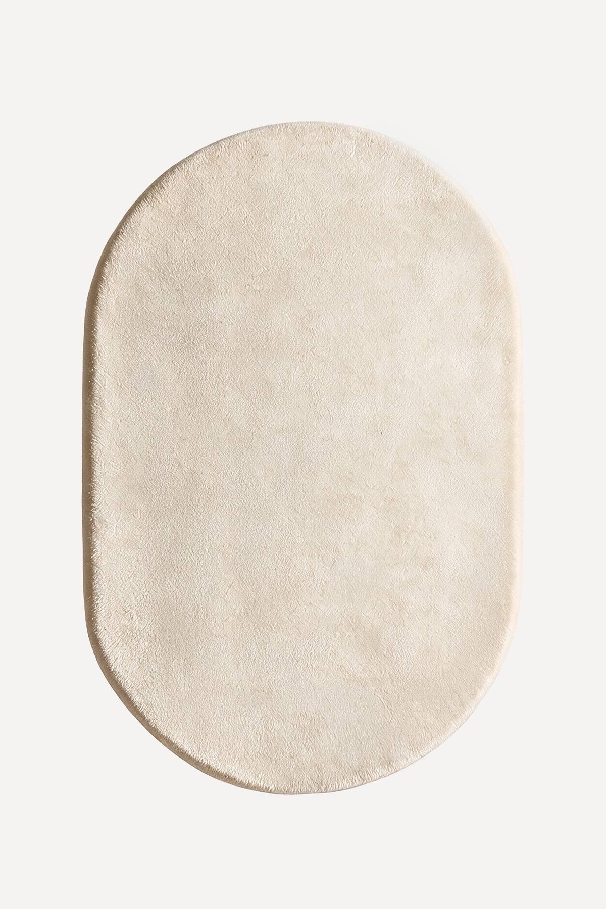 An oval-shaped cream-colored plush rug with a soft, textured surface, shown from a top-down view on a solid off-white background.