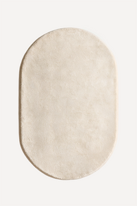 An oval-shaped cream-colored plush rug with a soft, textured surface, shown from a top-down view on a solid off-white background.