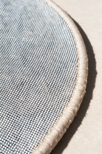 Close-up of a round rug corner showing a gray woven pattern with a thick cream fringed edge on a neutral background | Cotton backing