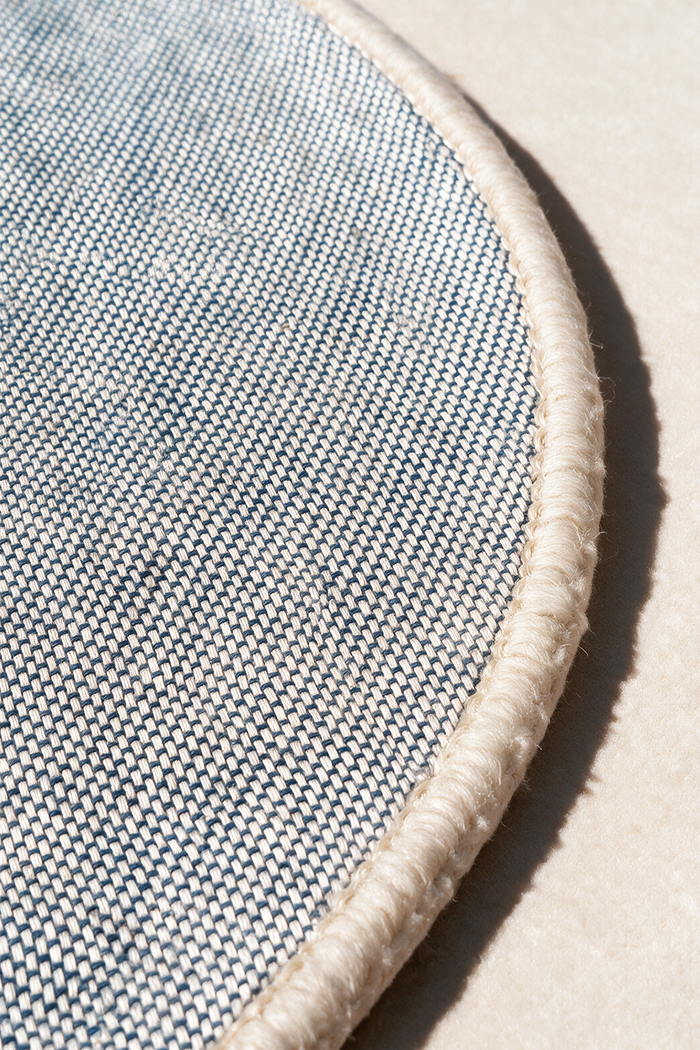 Close-up of a round rug corner showing a gray woven pattern with a thick cream fringed edge on a neutral background | Cotton backing